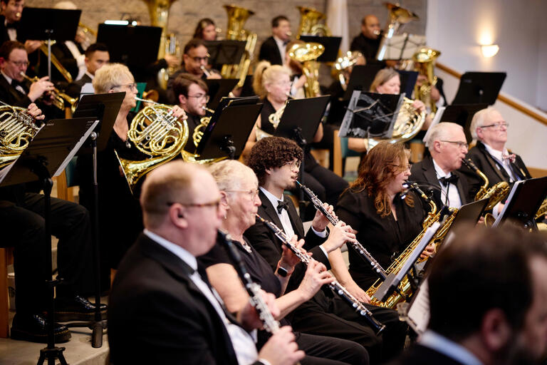 Dozens of musicians in formal outfits play instruments.